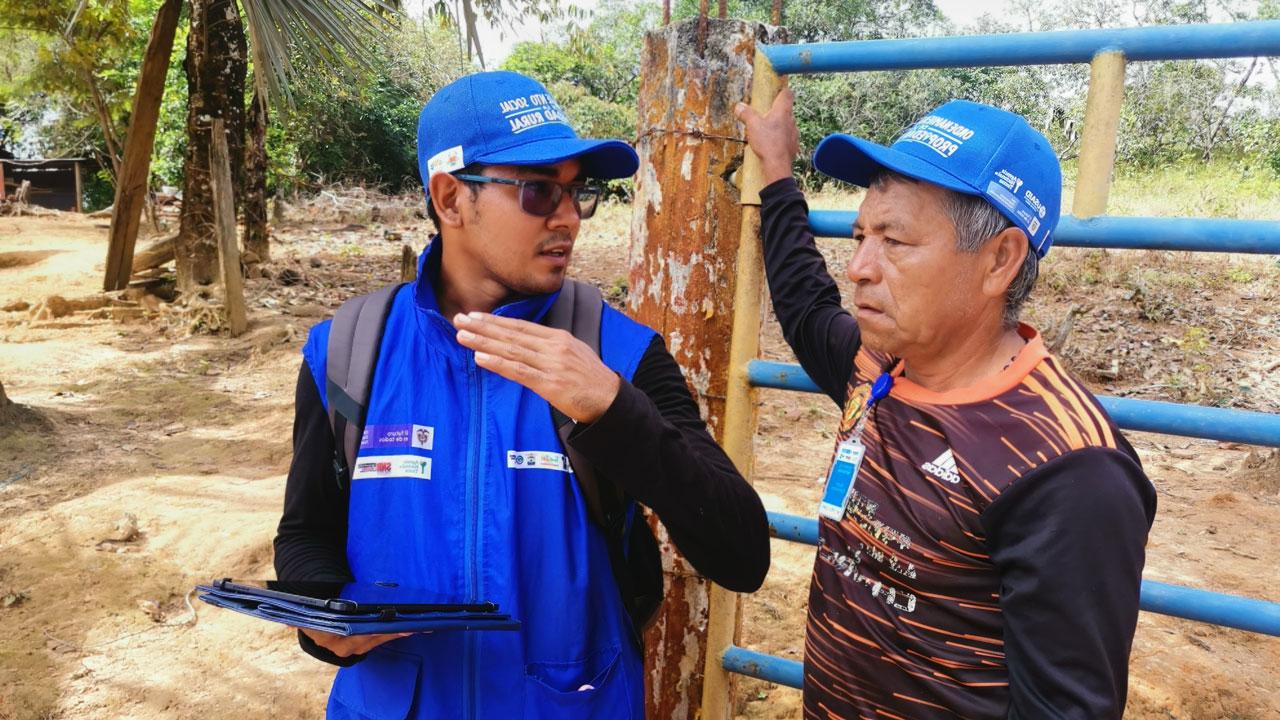 One man talks with his hands to explain something to another man, standing and holding onto a pole